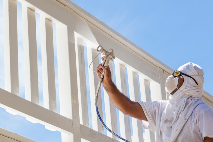 Hombre usando equipo protector pintando la reja de una terraza