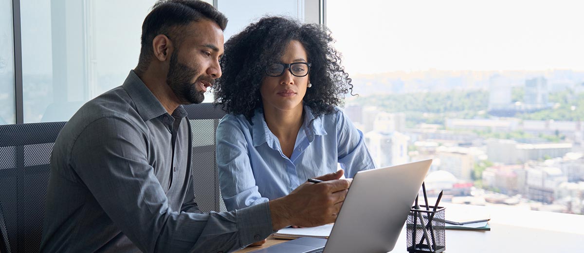 Man and woman at a desk looking at a laptop. They are wearing office clothing and working on a financial project.