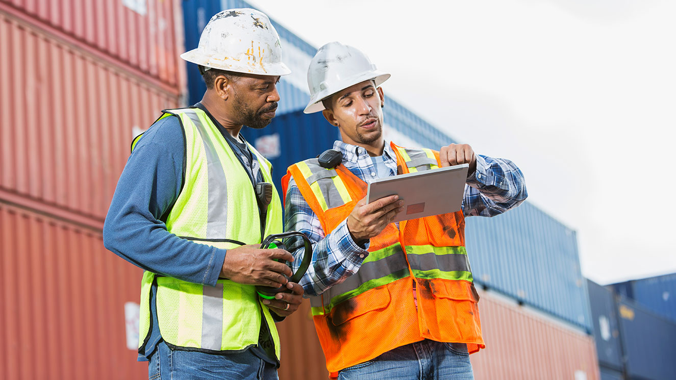 Two construction workers wearing bright vests and hard hats