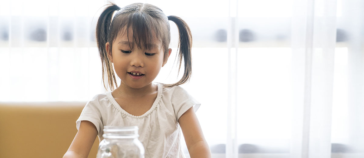 Niña sonriendo al poner monedas en un frasco.