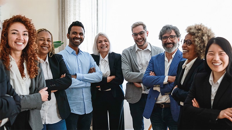 A diverse group of professionals pose for the camera, smiling and laughing.