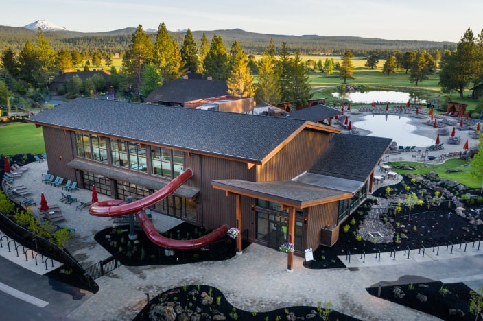 Aerial view of a resort lodge with a pool, plus a golf course in the distance.