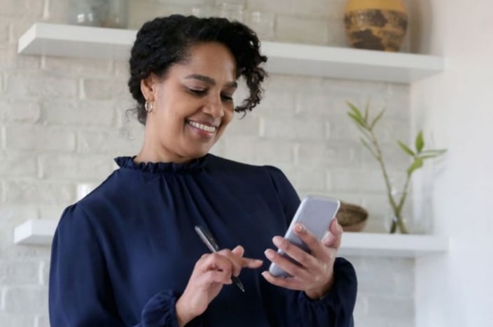 Photo of a woman with her phone in her hand and using it to pay a bill.