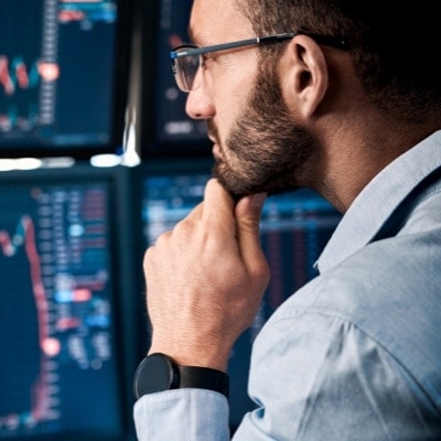 Person with their hand grabbing their chin while looking at computer monitors