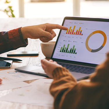 Two people looking and pointing at a chart on a laptop.