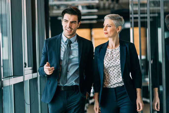 Man and woman dressed professionally walking together down a hallway in a large office building.