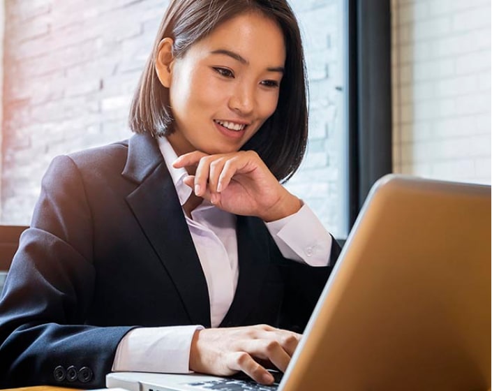 Woman in a business suit working on a computer near a window.