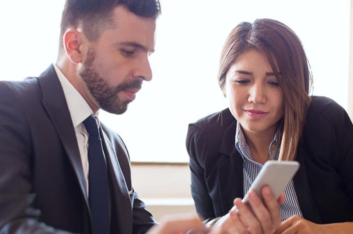 Man and woman looking at a cell phone and discussing a payment.