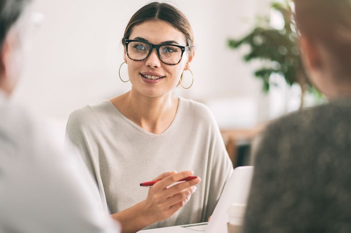 Woman wearing glasses presenting a business idea to two people.