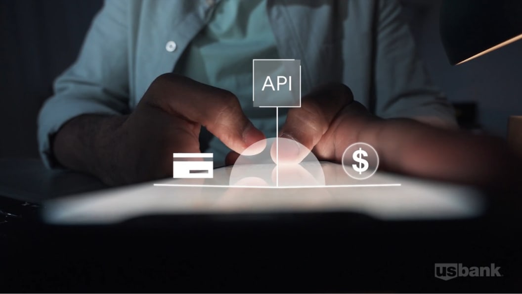 Close up shot of a pair of hands using a touchscreen tablet, then there is an illustration overlayed on top of the hands showing an illustration of a credit card, a dollar sign and a square with API written in it. 