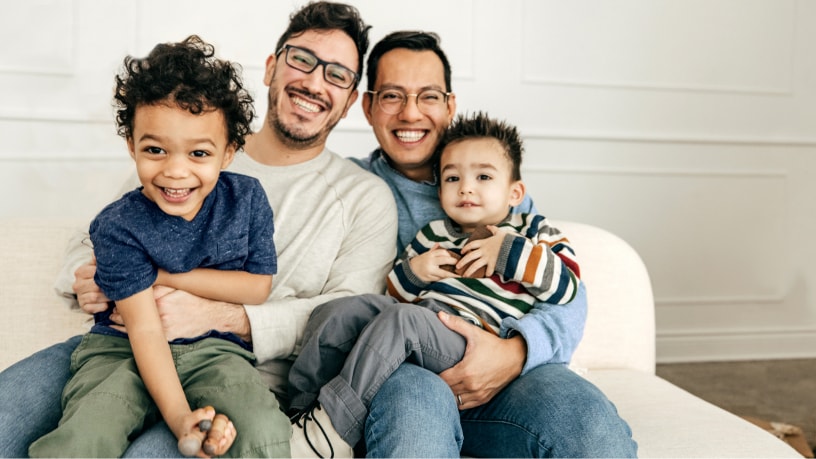 A male couple poses with their two children on their laps.