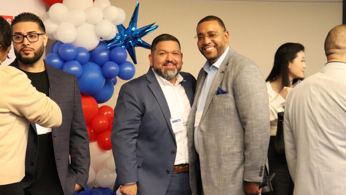 Two men posing for a photo against a backdrop of red and white and blue balloons