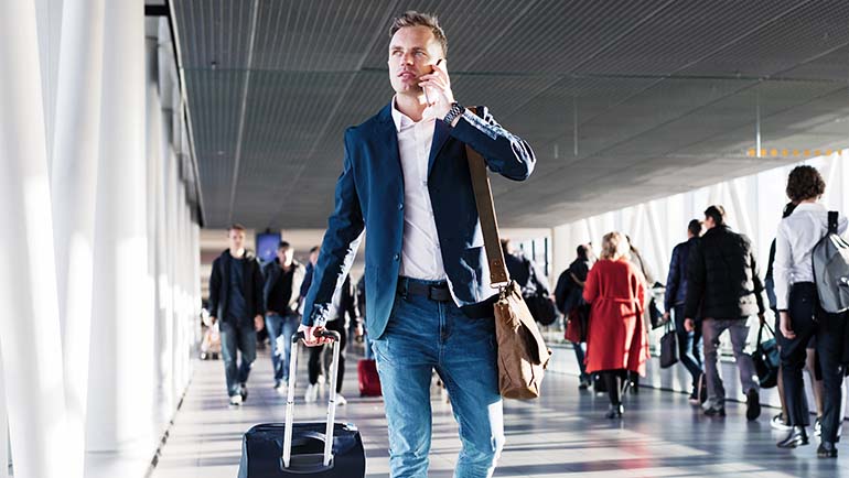 Man on cell phone walking through airport with a suitcase.