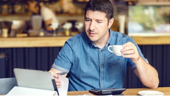 Man at a desk drinking coffee while reviewing paperwork.