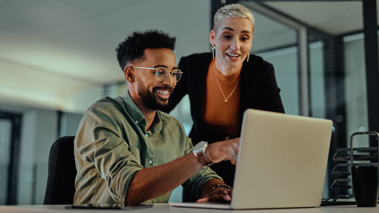 Male and female coworker in an office and reviewing accounting information on a laptop.