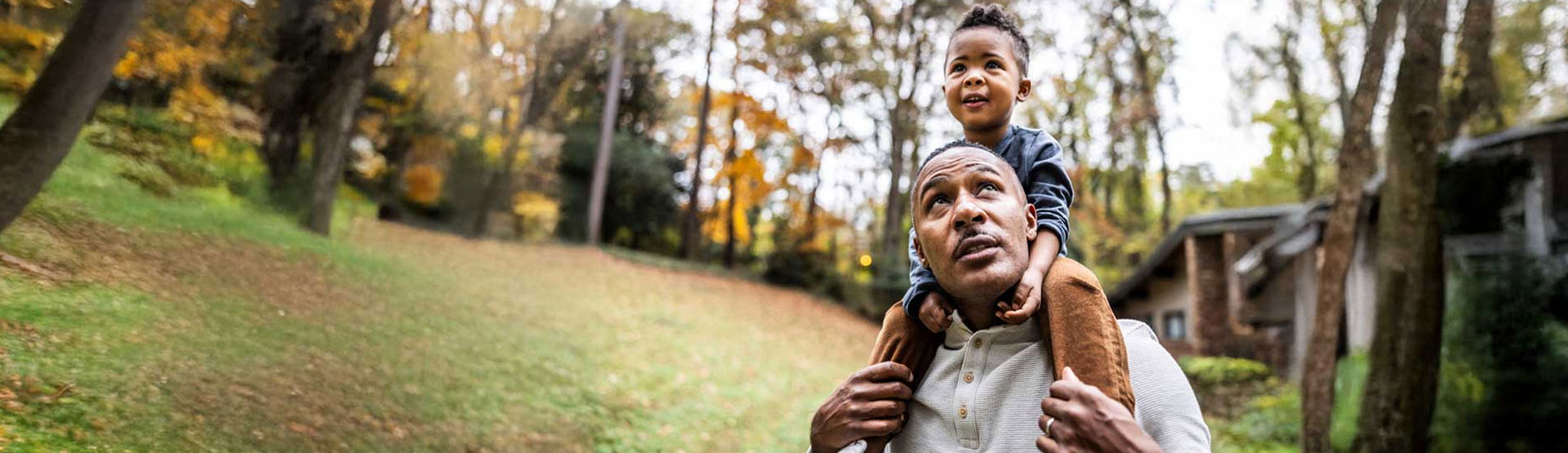 Black father with child sitting on his shoulders outside in nature.