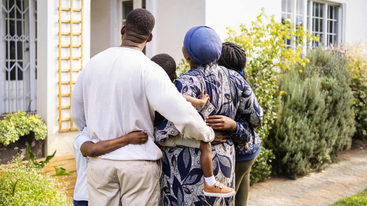 Family standing together with arms around each other looking at their home