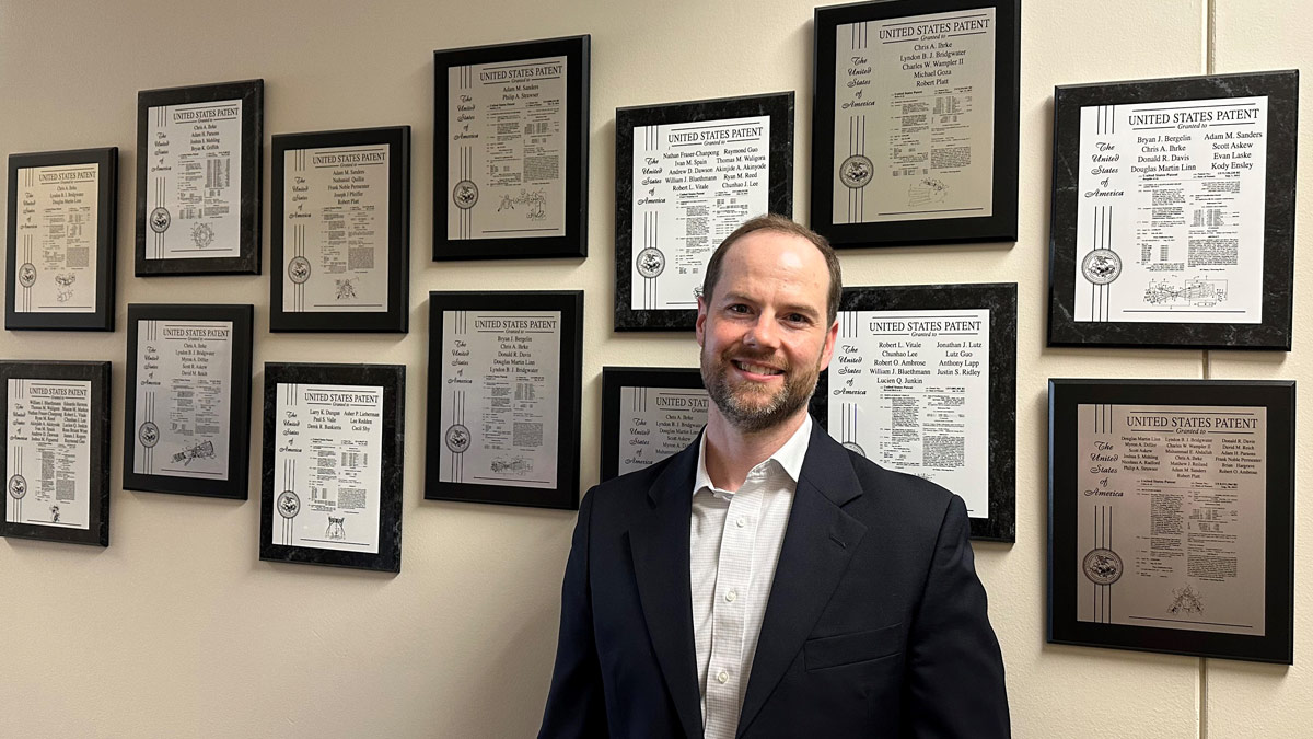 Man in front of framed patents hanging on a wall.