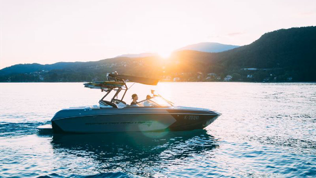 Two people on a boat with a sunset and mountains in the distance.  