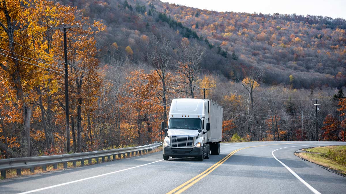 Semi-truck driving past blooming trees. 
