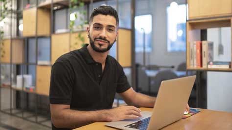 Male office worker sitting at table with laptop.