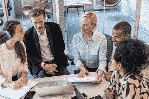 Five office workers around a table looking at papers for a presentation. 