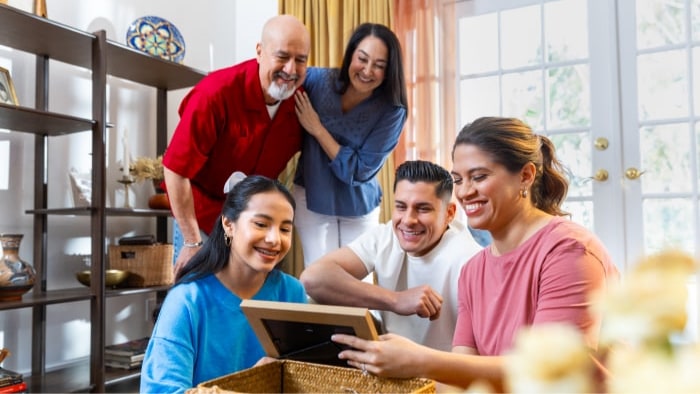 Three generations of a Hispanic family are in their living room looking over family photos.